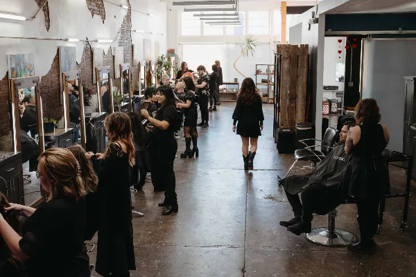 Interior view of a hair salon with multiple stylists working on clients in a spacious, industrial-style room.