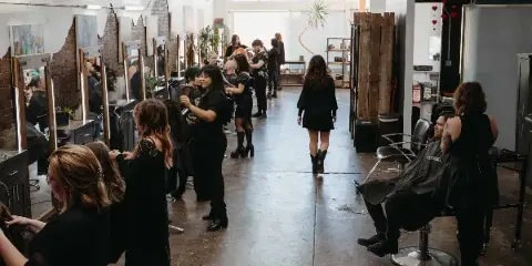 Interior view of a hair salon with multiple stylists working on clients in a spacious, industrial-style room.