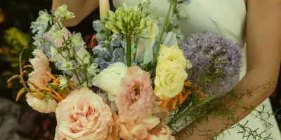A bride in a white dress holding a pastel-colored floral bouquet with roses and greenery.