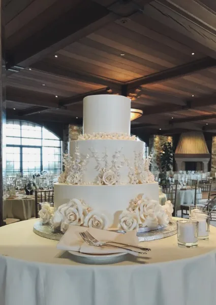 A three-tiered white wedding cake with floral decorations on a table in a banquet hall.