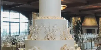 A three-tiered white wedding cake with floral decorations on a table in a banquet hall.