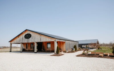 Exterior view of a large barn-style wedding venue with a gravel driveway and open sky.