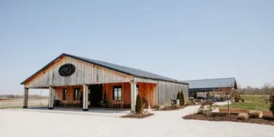 Exterior view of a large barn-style wedding venue with a gravel driveway and open sky.