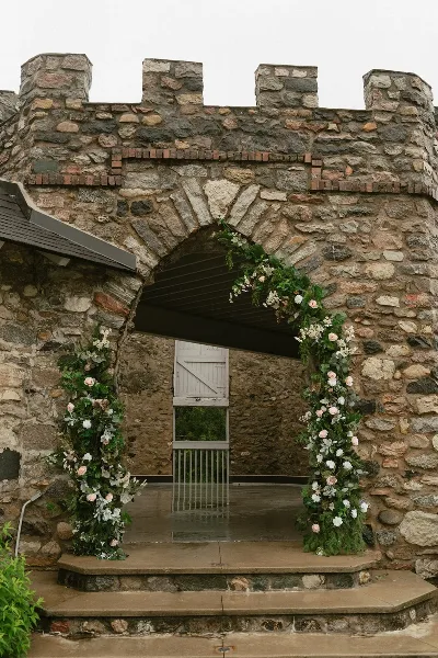 A stone archway decorated with a floral installation featuring greenery and white and pink flowers.