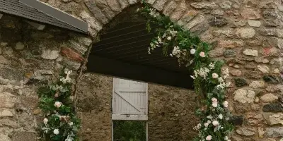 A stone archway decorated with a floral installation featuring greenery and white and pink flowers.