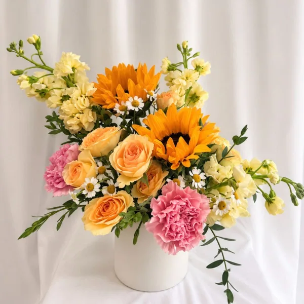 A mixed bouquet of sunflowers, roses, carnations, and small daisies in a white vase