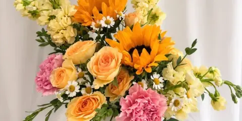 A mixed bouquet of sunflowers, roses, carnations, and small daisies in a white vase