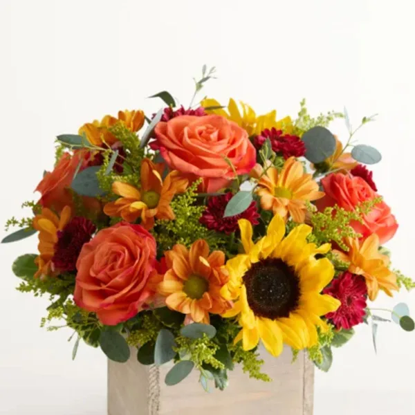 A floral arrangement with orange roses, sunflowers, and red daisies in a box
