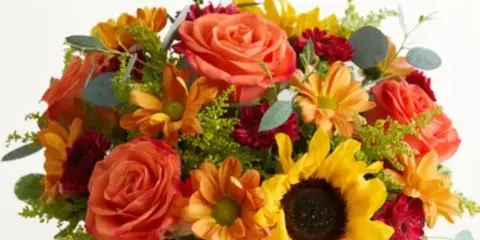 A floral arrangement with orange roses, sunflowers, and red daisies in a box
