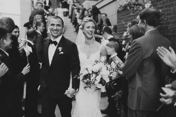 A bride and groom holding hands and smiling as they walk down the aisle during a wedding ceremony.