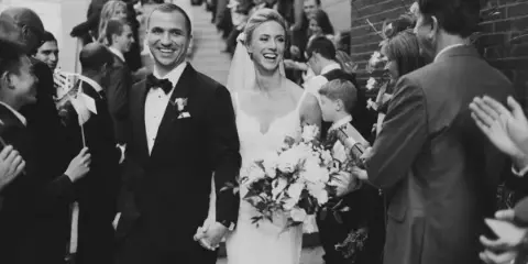 A bride and groom holding hands and smiling as they walk down the aisle during a wedding ceremony.
