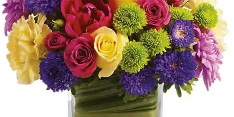 A colorful mixed bouquet of roses, chrysanthemums, and other flowers arranged in a clear glass vase.