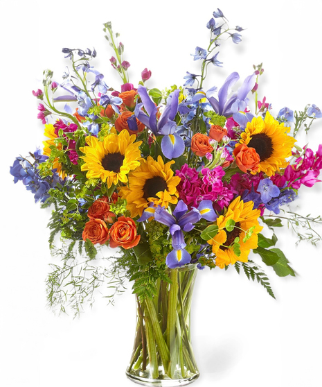 A colorful floral arrangement featuring sunflowers, irises, and roses in a clear glass vase.