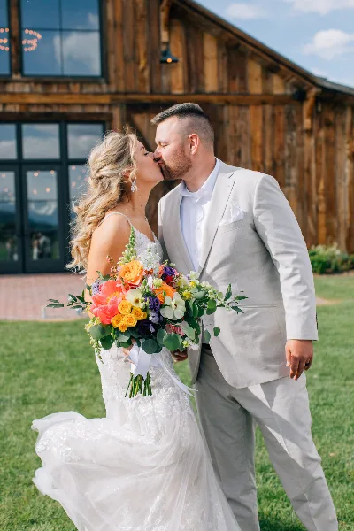 A bride and groom kissing outdoors in front of a rustic wooden building.