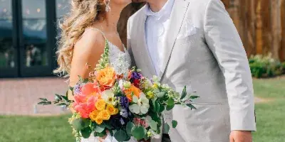 A bride and groom kissing outdoors in front of a rustic wooden building.