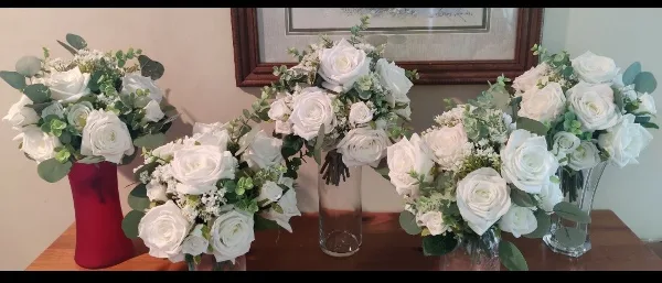 A set of white rose and eucalyptus floral arrangements displayed in vases on a wooden table.