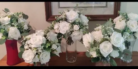 A set of white rose and eucalyptus floral arrangements displayed in vases on a wooden table.