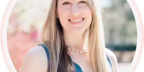 Portrait of a smiling woman with long blonde hair wearing a dark blue top and a gold necklace.