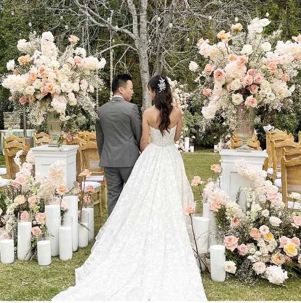 A bride and groom standing at an outdoor wedding altar decorated with large floral arrangements and candles.