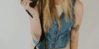 A smiling woman with long blonde hair holding a professional camera with a large lens.