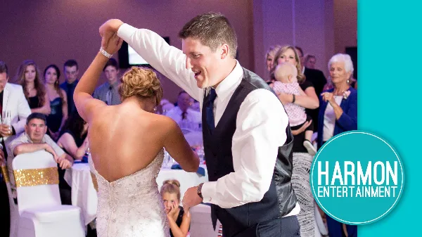 A bride and groom dancing at a wedding reception with guests in the background, featuring the Harmon Entertainment logo.
