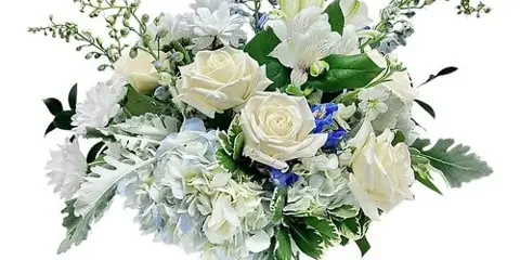 A white and blue floral arrangement featuring roses, hydrangeas, and lilies in a glass vase.