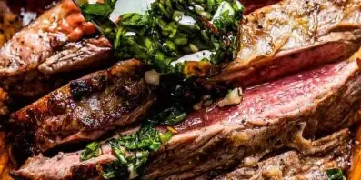 Sliced grilled meat with a fresh herb sauce being poured over it.
