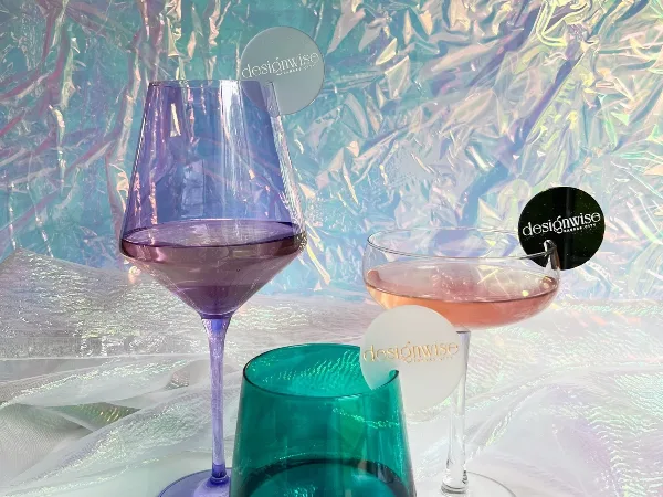 A close-up of purple and green glassware with designwise branded stirrers set against a textured, iridescent backdrop.