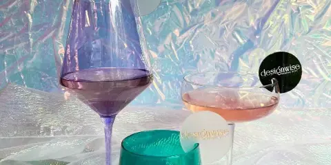 A close-up of purple and green glassware with designwise branded stirrers set against a textured, iridescent backdrop.