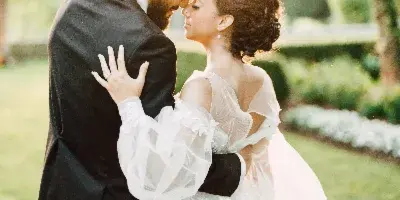 A bride and groom embracing outdoors in a garden setting with sunlight filtering through the trees.
