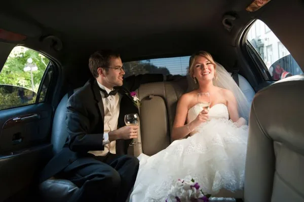 A bride and groom sitting in the back seat of a limousine holding champagne glasses.