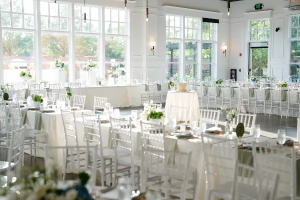 Interior view of a wedding venue banquet hall with white tables, chairs, and floral arrangements.