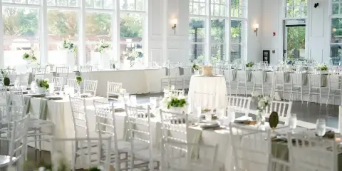 Interior view of a wedding venue banquet hall with white tables, chairs, and floral arrangements.