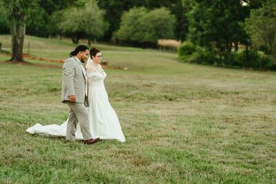 A bride and groom standing together in a grassy field with trees in the background.