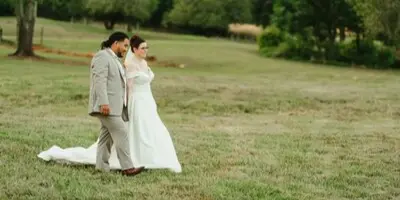 A bride and groom standing together in a grassy field with trees in the background.