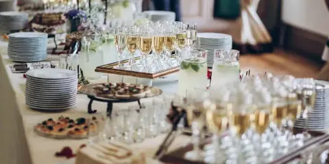 A catering table set with champagne flutes, hors d'oeuvres, and stacked plates.