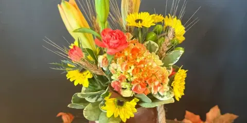 Autumn floral arrangement in a rope-wrapped vase with yellow blooms and orange lilies