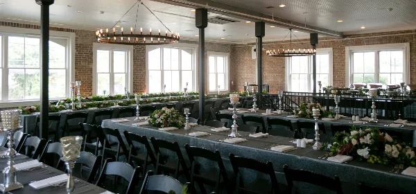 Decorated event venue with long tables, floral arrangements, candle holders, and chandeliers.