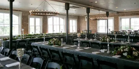 Decorated event venue with long tables, floral arrangements, candle holders, and chandeliers.