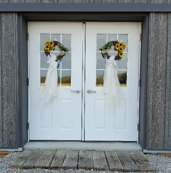 White double doors with sunflower wreaths on a rustic wooden building exterior