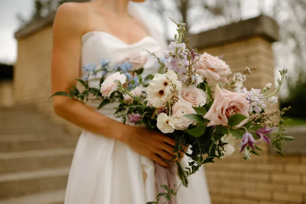 Close-up of a bride holding a lush bouquet of pink and white roses with greenery.