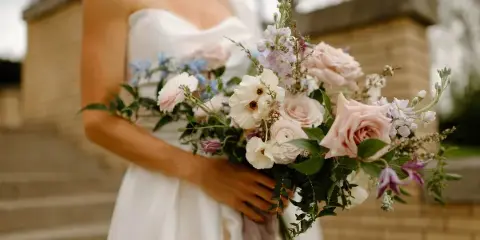 Close-up of a bride holding a lush bouquet of pink and white roses with greenery.
