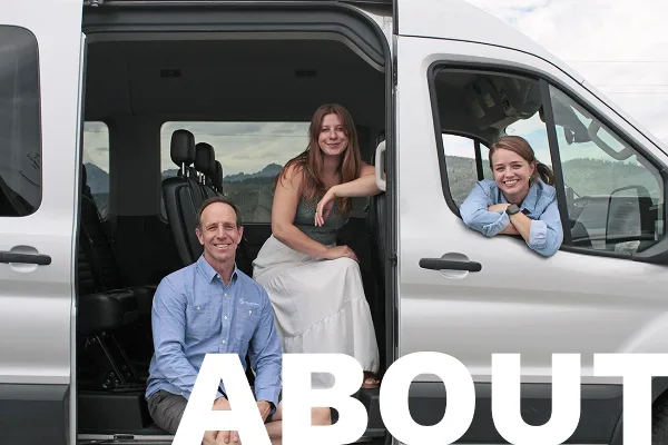 Three smiling staff members posing with a white passenger van