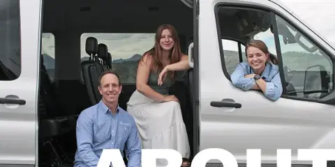 Three smiling staff members posing with a white passenger van