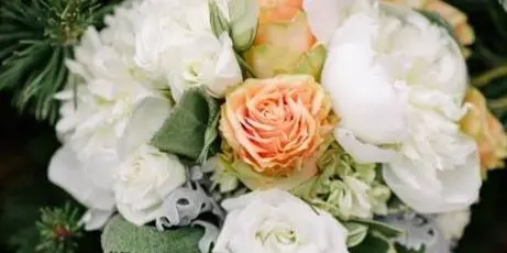 A close-up photograph of a floral bouquet featuring white and peach roses, white hydrangeas, and greenery.