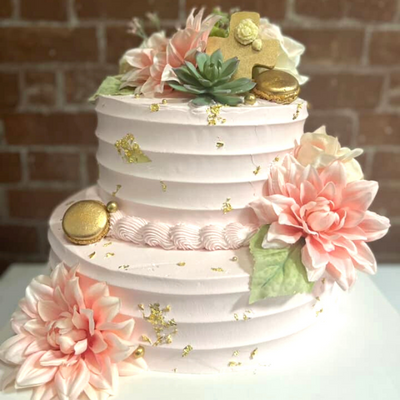 A three-tiered white wedding cake decorated with pink and white flowers, succulents, and gold accents.