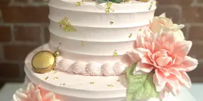 A three-tiered white wedding cake decorated with pink and white flowers, succulents, and gold accents.