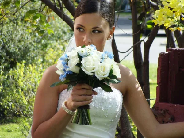 A bride in a white wedding dress holding a bouquet of white roses and blue flowers.