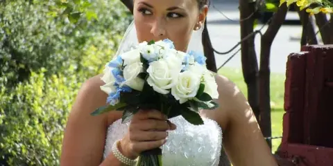A bride in a white wedding dress holding a bouquet of white roses and blue flowers.