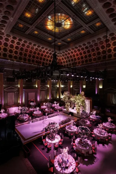 Interior view of a grand ballroom with a stained glass ceiling, marble columns, and round tables set for a formal event.